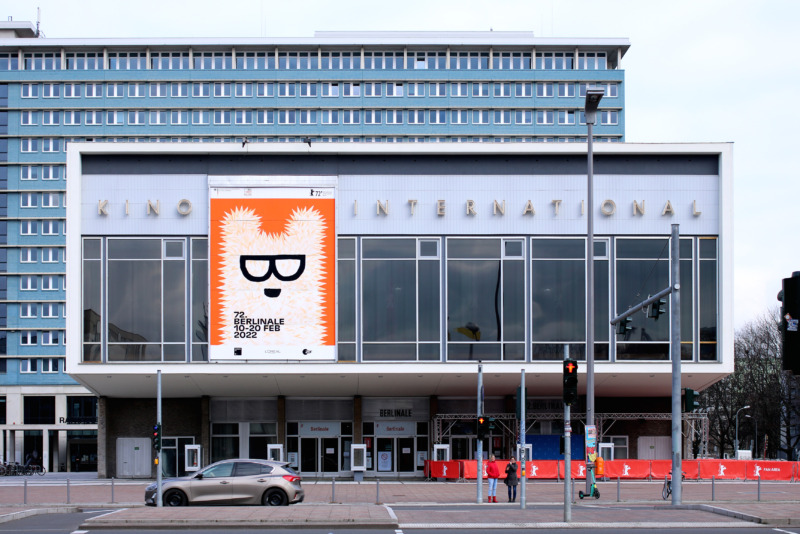Exterior view of the Kino International in Berlin with a large orange-and-white Berlinale poster showing a bear wearing glasses.