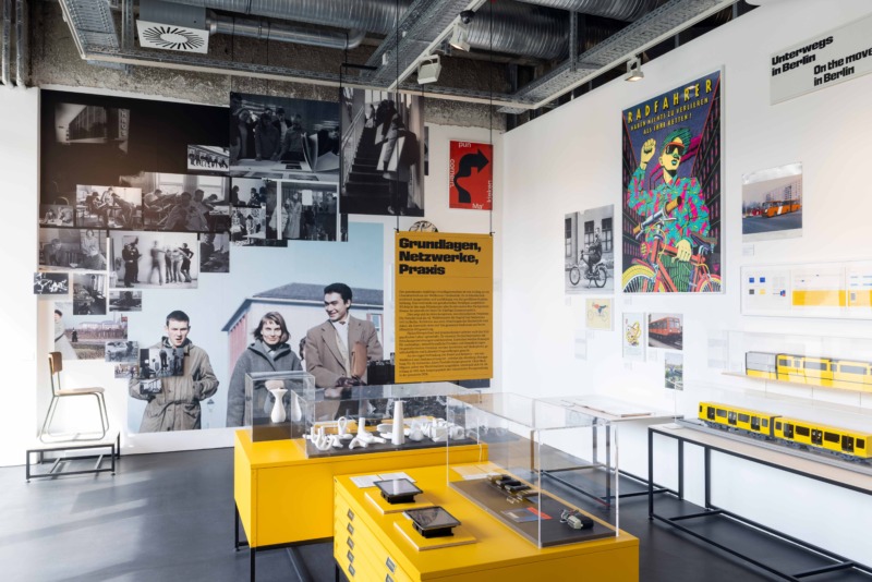 Exhibition view featuring photographs, graphic works, posters, and text panels in a modern museum space