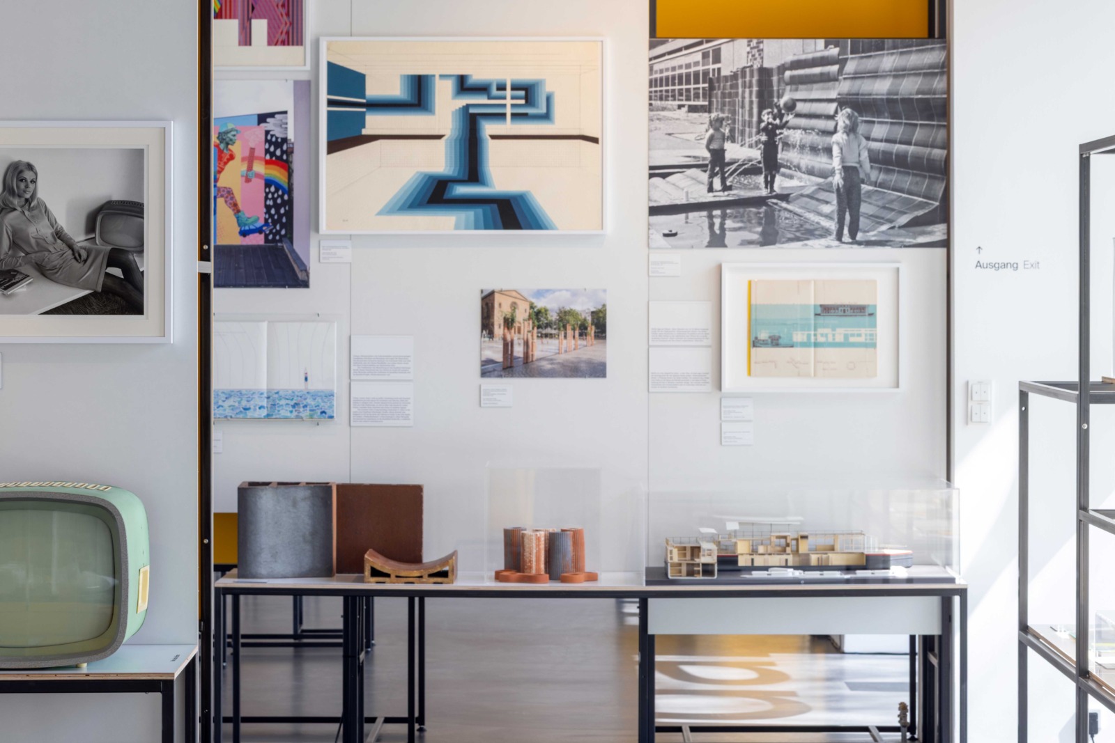 Exhibition view featuring photographs, graphic works, posters, and text panels in a modern museum space