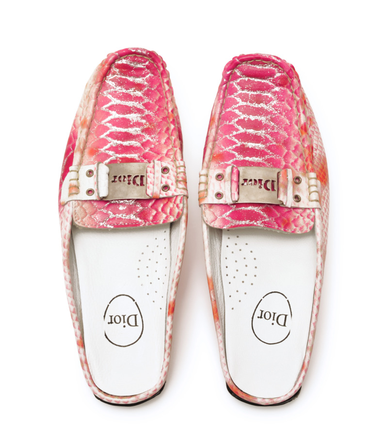 A pair of counterfeit Dior slip-ons in a pink snakeskin-effect finish, featuring silver glitter details and a logo buckle.