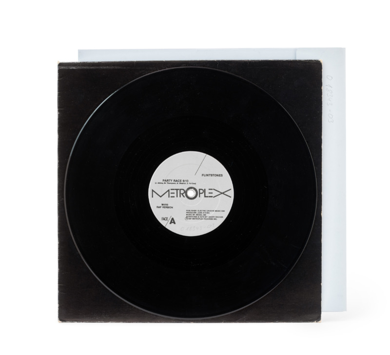 A black vinyl record with a white Metroplex label on top of a black inner sleeve and a white outer envelope.